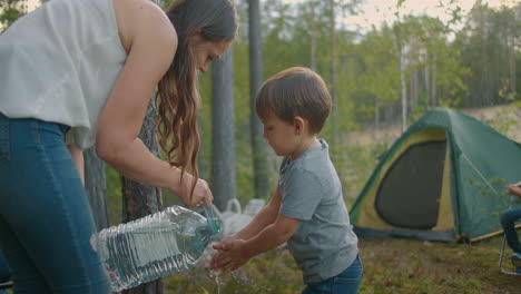 child-is-washing-hands-in-forest-hike-mother-is-pouring-water-from-bottle-family-camp-in-reserve-at-weekend